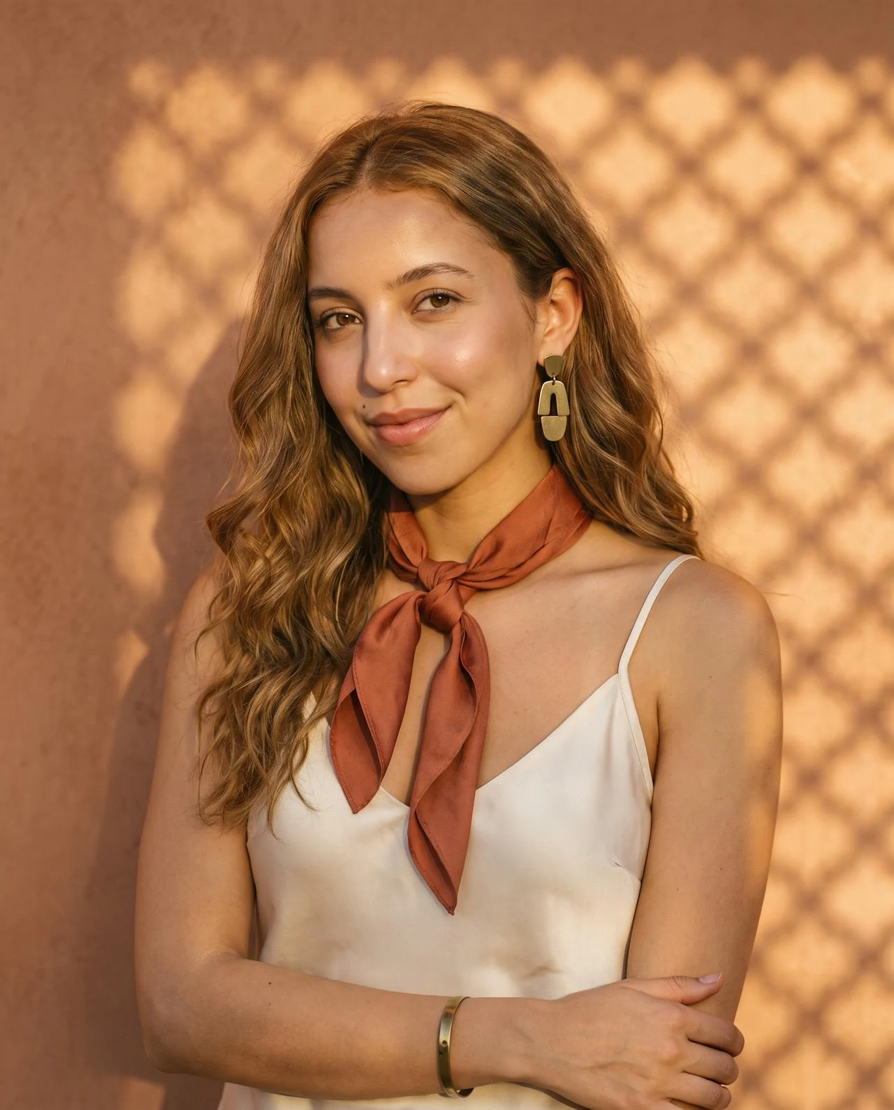 Une femme en haut satiné crème, foulard terracotta noué au cou et boucles géométriques en laiton